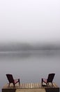 Pair of Adirondack chairs on wooden deck on lake in fog with copy space Royalty Free Stock Photo