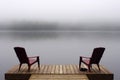 Pair of Adirondack chairs on wooden deck on lake in fog with copy space Royalty Free Stock Photo