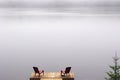 pair of Adirondack chairs on wooden deck on lake in fog with copy space Royalty Free Stock Photo