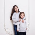 Two adorabile littles girl in sweater and jeans, posing together embraced on white background. Royalty Free Stock Photo