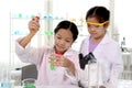 Two Adorable Asian schoolgirls in lab coat doing science experiments, happy smiling girl kid adding chemical to green test tube Royalty Free Stock Photo