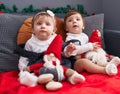 Two adorable babies sitting on sofa playing with santa claus doll at home Royalty Free Stock Photo