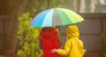 Two adorable children, boy and girl playing in park with colorful rainbow umbrella on a rainy autumn day. Child in Royalty Free Stock Photo