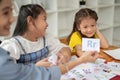 Two adorable young Asian girls are enjoying studying English alphabet flashcards with a teacher