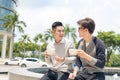 Two adult male friends sit talking over coffee outside cafe