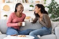 Two african besties laughing while drinking tea together at home