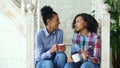 Two african american curly girls sistres sitting on stairs have fun laughing and chatting together at home Royalty Free Stock Photo