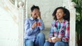 Two african american curly girls sistres sitting on stairs have fun laughing and chatting together at home Royalty Free Stock Photo