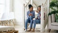 Two african american curly girls sistres sitting on stairs have fun laughing and chatting together at home Royalty Free Stock Photo