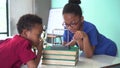 Two African American mixed kids using a magnifying glass and pulling a newton`s cradles ball swing in science classroom