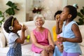 Two african american sisters blowing bubbles while grandmother and mother watching sitting on couch