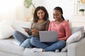 Two african female friends spending time at home, using gadgets