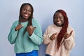 Two african woman standing over blue background pointing to the back behind with hand and thumbs up, smiling confident Royalty Free Stock Photo