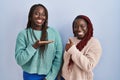 Two african woman standing over blue background showing palm hand and doing ok gesture with thumbs up, smiling happy and cheerful Royalty Free Stock Photo