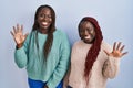 Two african woman standing over blue background showing and pointing up with fingers number ten while smiling confident and happy Royalty Free Stock Photo