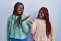 Two african woman standing over blue background smiling showing both hands open palms, presenting and advertising comparison and Royalty Free Stock Photo