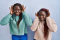 Two african woman standing over blue background trying to hear both hands on ear gesture, curious for gossip Royalty Free Stock Photo