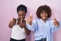 Two african women standing over pink background approving doing positive gesture with hand, thumbs up smiling and happy for Royalty Free Stock Photo