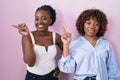 Two african women standing over pink background with a big smile on face, pointing with hand finger to the side looking at the Royalty Free Stock Photo