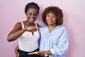 Two african women standing over pink background gesturing with hands showing big and large size sign, measure symbol Royalty Free Stock Photo