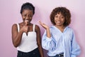 Two african women standing over pink background showing palm hand and doing ok gesture with thumbs up, smiling happy and cheerful Royalty Free Stock Photo