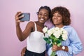 Two african women taking a selfie photo with flowers smiling with a happy and cool smile on face Royalty Free Stock Photo