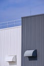 Two air ducts ventilation on grey and white corrugated metal factory buildings wall with blue sky background Royalty Free Stock Photo