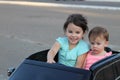 Two amazing girls ride in one big toy car on city street asphalt. Outdoor driving in a summer attraction for children Royalty Free Stock Photo