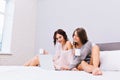 Two amazing joyful girls in warm woolen sweaters with naked long legs surfing in internet on bed. Good morning of young