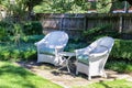 Two antique white wicker chairs arranged with table in shady spot in landscaped yard in upscale urban neighborhood Royalty Free Stock Photo