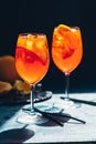 Two Aperol spritz cocktail in big wine glass with oranges, summer Italian fresh alcohol cold drink. Dark bar counter background