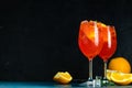 Two Aperol spritz cocktail in big wine glass with oranges, summer Italian fresh alcohol cold drink. Dark bar counter background