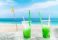 Two apple green drift-ice with straw on the beach. In the background is blue sky, palms, sea nd sandy beach. This is situated in