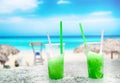 Two apple green drift-ice with straw on the beach. In the background is blue sky, palms, sea nd sandy beach. This is situated in