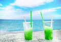 Two apple green drift-ice with straw on the beach. In the background is blue sky, palms, sea nd sandy beach. This is situated in