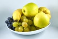 Two apples, a banana, a quince, white grapes, black grapes on a white plate Royalty Free Stock Photo