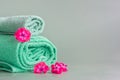 Two aquamarine towels lie on a gray-green background along with pink flowers.Rolled face cloths Royalty Free Stock Photo