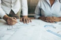 Two architect working at construction site and compass drawing pointing on blueprint with partnership