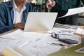 Two architects working and discussing construction blueprint with laptop computer and engineering tools on table in office Royalty Free Stock Photo