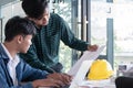 Two architects working and discussing construction blueprint with laptop computer and engineering tools on table in office Royalty Free Stock Photo