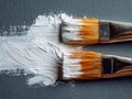 Two artist paintbrushes applying thick white paint strokes on a gray textured surface creating a dynamic pattern in close-up Royalty Free Stock Photo