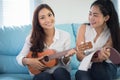 Two asia women are having fun playing ukulele and smiling at home for relax time