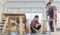 Two asian adult carpenters wearing plaid shirt smiling happily assemble wooden desk together by using electric screwdriver and