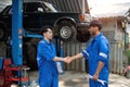 Two Asian automotive mechanic repairman handshake in garage. Vehicle service manager working in mechanics workshop, feel