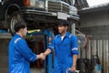 Two Asian automotive mechanic repairman handshake in garage. Vehicle service manager working in mechanics workshop, feel