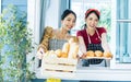 Two Asian beautiful female friends wearing aprons, standing and while opening window, welcome, happily smiling, serving breakfast