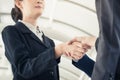 Two asian businessmen shaking hands after seal a deal in the meeting and their staff team congratulation on background.