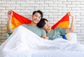 Two Asian cheerful lovely pride male gay men lover couple partner smiling sitting holding hands together in bed under colorful Royalty Free Stock Photo