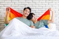 Two Asian cheerful lovely pride male gay men lover couple partner smiling sitting holding hands together in bed under colorful Royalty Free Stock Photo