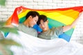 Two Asian cheerful lovely pride male gay men lover couple partner smiling sitting holding hands together in bed under colorful Royalty Free Stock Photo